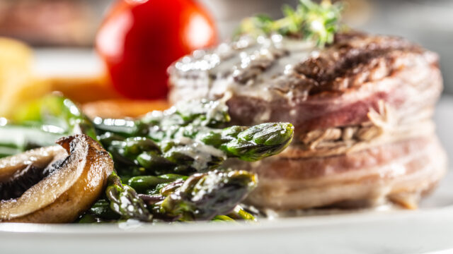 Grilled steak served on a plate with asparagus, potatoes and tomato.